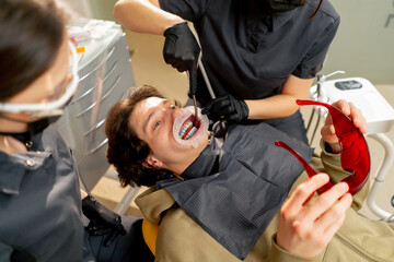 dental office girl dentist applies protective gel to the gums of young guy