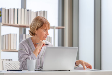 Woman using laptop and smartphone at home, Mature woman checking their bills