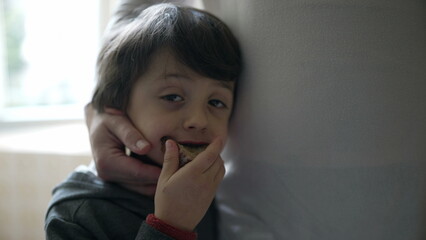 Small boy eating slice of bread while receiving affection from mother's hand. Close-up of 5 year...