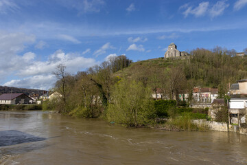 Fototapeta na wymiar View of a swollen River Meuse at Dun-sur-Meuse, in the Meuse Valley in France. The church of Our Lady is visible in it's prominent hill top location.