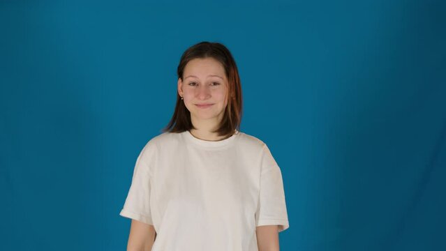 Funny young woman turns head making dab movement. Happy lady in t-shirt makes gesture expressing playfulness on blue blackground