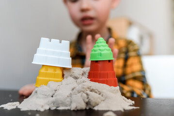 A child makes a tower of kinetic sand at home. Boy playing in the sandbox