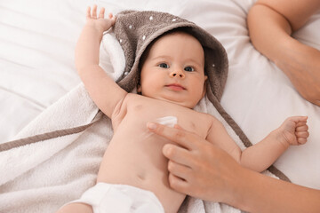 Woman applying body cream onto baby`s skin on bed, closeup