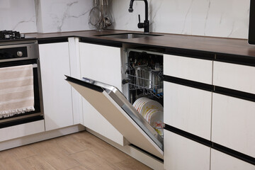 Open modern dishwasher with dirty tableware in kitchen