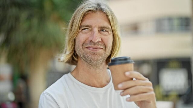 Handsome man with blond long hair holding coffee cup on city street.