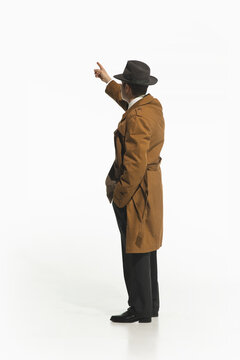 Man in retro-style trench coat and fedora hat standing and pointing upwards isolate don white background. Concept of retro and vintage, fashion, business, detective