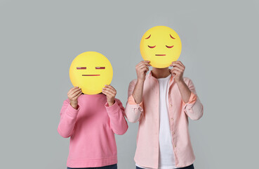 People covering faces with sad emoticons on grey background