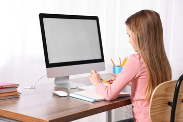 E-learning. Cute girl taking notes during online lesson at table indoors