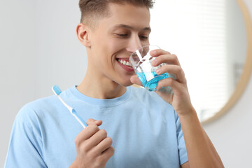 Young man using mouthwash in bathroom. Oral hygiene