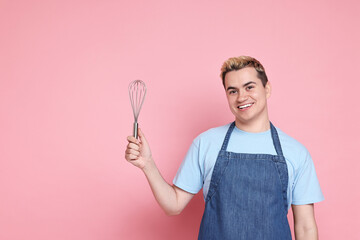 Portrait of happy confectioner holding whisk on pink background, space for text