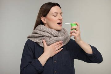 Woman with scarf using throat spray on grey background