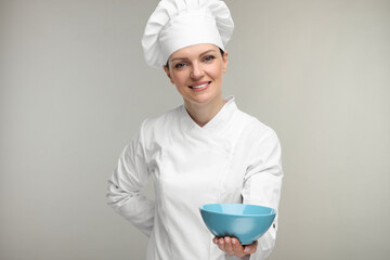 Happy chef in uniform holding bowl on grey background