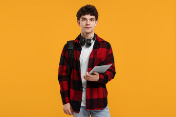 Portrait of student with backpack, headphones and tablet on orange background