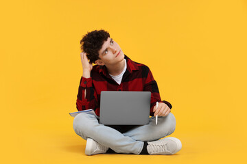 Portrait of student with laptop and pen on orange background