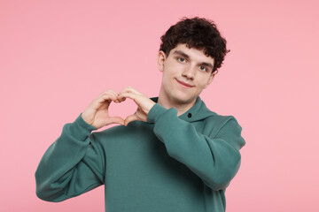 Happy young man showing heart gesture with hands on pink background