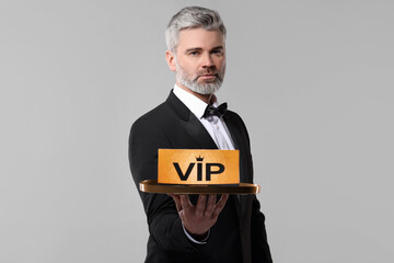 Handsome man holding tray with VIP sign on light grey background
