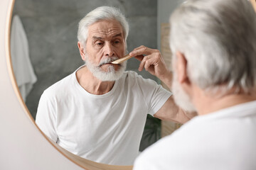 Senior man combing mustache near mirror in bathroom