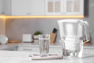 Water filter jug and glass on white marble table in kitchen, closeup. Space for text