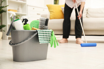 Woman cleaning floor, focus on different supplies in bucket at home