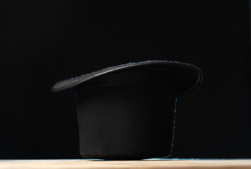 Magician's hat on wooden table against black background