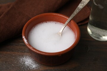 Chemical reaction of vinegar and baking soda in bowl on wooden table, closeup