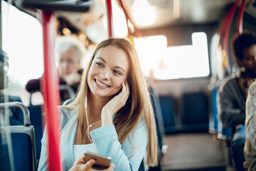 Smiling woman listening to music on her phone while on the bus