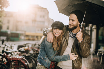 Loving couple sharing an umbrella on a sunny rain day in the city