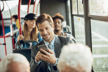 Smiling young adult businessman using smartphone on the bus