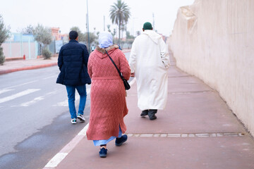 people walk along high wall Red City Marrakech hurry about business, authentic urban African...