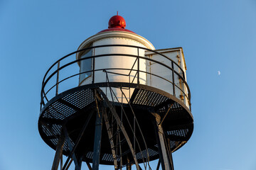 A beautiful white and red lighthouse on the North Sea coast in the Netherlands. Lighthouse against the blue sky. Beautiful metal construction.