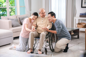 Happy elder Asian man using wheelchair while exercise indoor house with his son taking care of him...