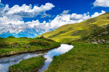 Fototapeta na wymiar Tranquil Mountain Stream Amidst Alpine Landscape with Green Meadows