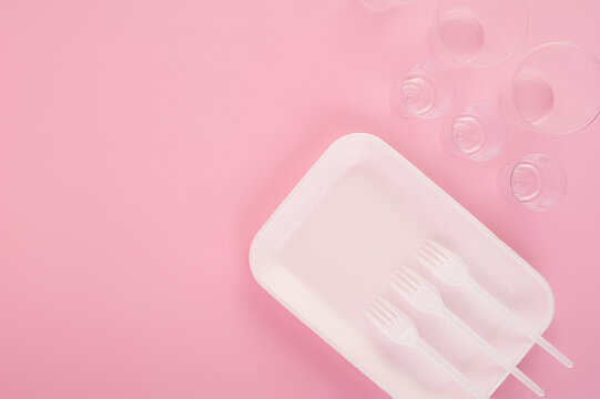 plastic disposable tableware on a pink background. Still life