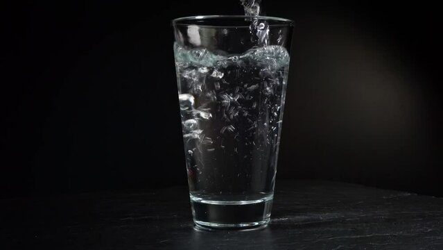 Pouring Water into a Glass and add Vitamin C effervescent tablet on black Background