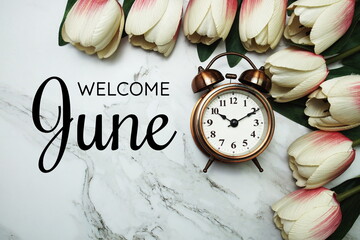 Welcome June text with alarm clock and tulip flower bouquet on marble background