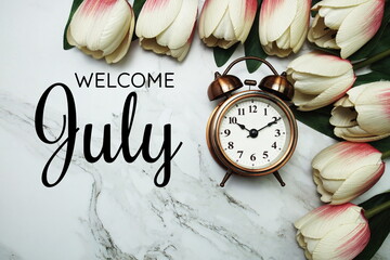 Welcome July text with alarm clock and tulip flower bouquet on marble background
