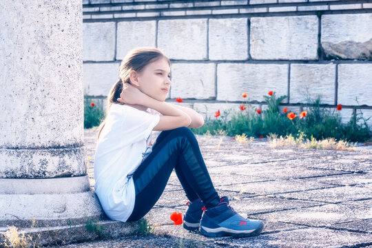 Portrait of a beautiful girl with a thoughtful look, seated at the base of a stone column and her hands resting on her knees.
