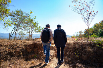 back view father and adult son with backpack walking to see scenic mountains in countryside,concept of family lifestyle,relationship,togetherness,holiday,travel