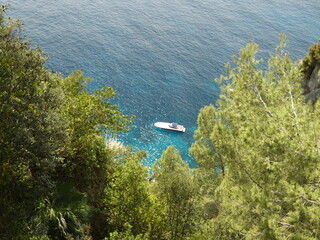 Sicht von der Klippe durch grüne Bäume auf ein Boot auf dem glänzenden Meer im türkisen Wasser