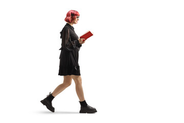 Full length profile shot of a young woman with red hair in a black dress walking and reading a book