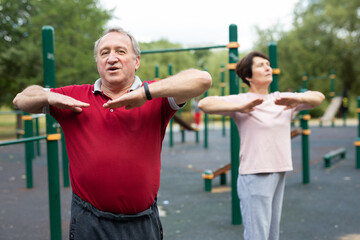 Elderly man and woman doing gymnastics on an outdoor sports ground