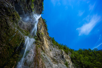 Waterfall hidden inside the forest, beauties of Slovenia to be discovered. Near Nova Gorica, Tolmin village. Water spray and vivid rainbow forms from the waterfall that falls sheer onto the rock.