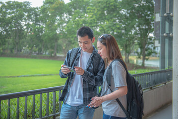 Two Asian male and female college students are using an application on their phone. To find additional information and communication channels to the concept of education and technology