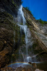 Waterfall hidden inside the forest, beauties of Slovenia to be discovered. Near Nova Gorica, Tolmin village. Water spray and vivid rainbow forms from the waterfall that falls sheer onto the rock.