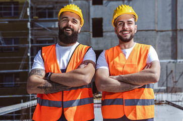 Portrait of construction workers on a construction site. Wearing yellow helmet and safety orange vest.