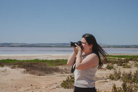 Woman in casual attire taking photos in a coastal landscape, embodying exploration and the joy of photography.