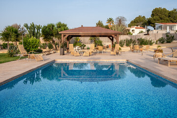 Reflective blue pool with a wooden pergola and lounging chairs in the background, symbolizing serene luxury and relaxation.