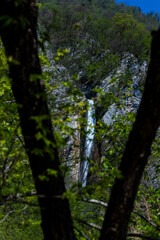 Fototapeta premium Gregorčičev Waterfall hidden inside the forest, beauties of Slovenia to be discovered. Near Nova Gorica, Tolmin village. Water spray, vivid rainbow forms from the waterfall that falls onto the rock.