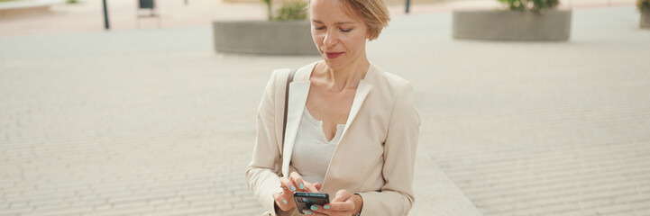 Businesswoman with blond hair sitting on a bench typing on cellphone on cellphone, Panorama