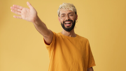 Close up, guy with glasses, dressed in yellow T-shirt, waving palm in greeting gesture looking at...